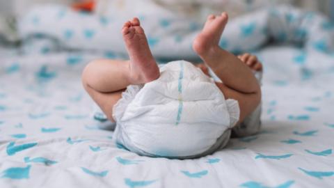 Newborn baby lying on a bed but view is of their raised legs and nappy