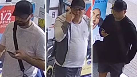 A picture of three people captured on CCTV footage inside of the store. The man on the left is wearing a white top, black bag and is holding a phone. He is also wearing a black cap and has a beard. The man pictured in the middle is wearing a white shirt, grey shorts and a grey jacket. He is also wearing a hat and holding a phone. The man pictured on the right - is wearing a black jumper, grey shorts and a black hat. He is also holding a phone in his hand.