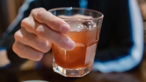 A close-up of an anonymous man holding a tumbler filled with dark alcohol and ice