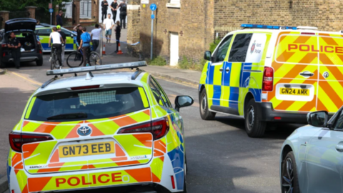 A police car and a police van parked in the area where the children went missing on Friday. A third police vehicle and some cordon can be seen in the distance.