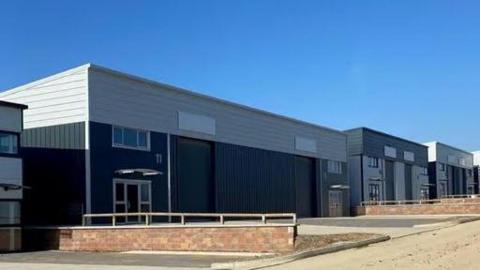 A grey and black warehouse with some parking spaces in front of it.