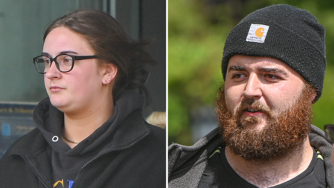 Sophie, left, wearing a black hoodie. She has black glasses and brown hair, with three earrings on her right ear. Jamie on the right has a black beanie hat on, and a large ginger beard. He is wearing a black coat
