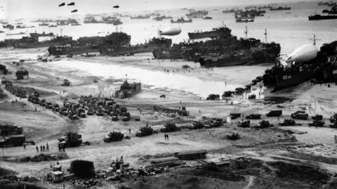 A black and white image of various naval vessels landing on the beaches of Normandy
