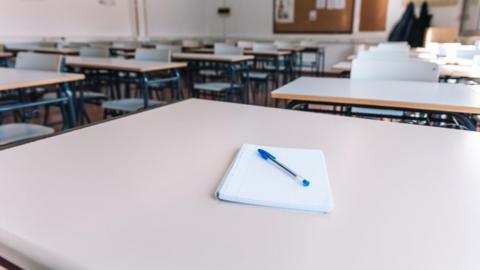 A generic picture of an classroom with a notepad and pen on a desk.