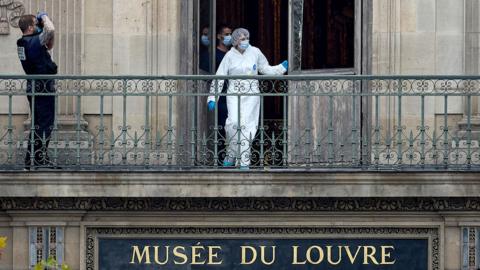 A forensic worker in white overall, gloves and mask exits the balcony door above a sign saying 'Musee du Louvre galeris des antiques' while another officer takes a photo of the scene, in Paris on 19 October.