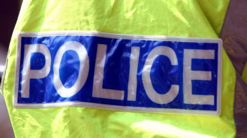 A yellow high-vis police jacket with police written in large white block capitals on a blue background.