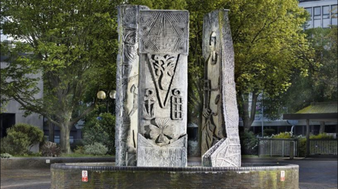 A concrete sculpture featuring three large decorated rectangular plinths standing opposite each other in a circular formation 