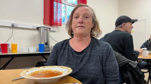 Roxanna Twidle with grey top on sitting with a bowl of soup