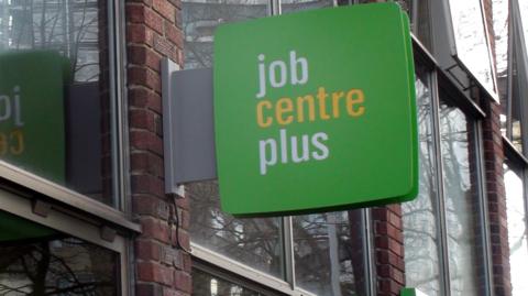 Jobcentre Plus sign on a building with a green background and writing in white and yellow