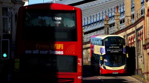 Two buses on either side of a road. A shadow covers half of one of the buses, on the left.