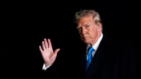 US President Donald Trump waves after exiting a plane at Joint Base Andrews