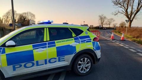 A police car parked across a road with traffic cones behind it