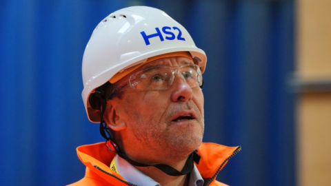 Wearing a white hard hat, safety goggles and an orange high visibility jacket, HS2 Ltd CEO Mark wild appears to be looking uptowards something out of shot as the camera takes his picture