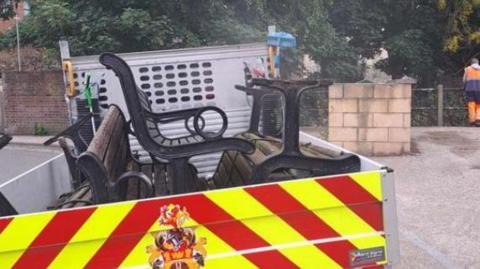 The four benches stacked in the back of a council truck, being driven away from the area