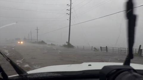 Flooded streets and grey skies are seen through a car's windscreen