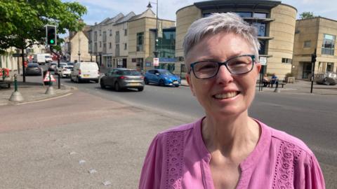Eugene Gooch looks into the camera, wearing glasses and pink top while standing in Calne town centre.