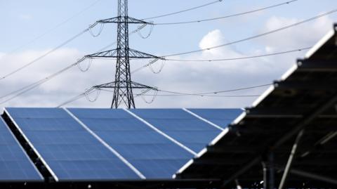 Solar panels installed with a high-voltage pole standing behind them. 