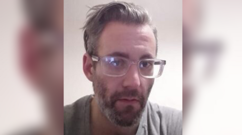 A picture of Michael Wheeler, who has a grey beard, grey T-shirt and glasses