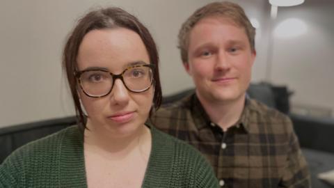 Mother Beth Cooper sitting close to the camera wearing a black blouse with her partner Tom Coxhead sitting just behind her.
