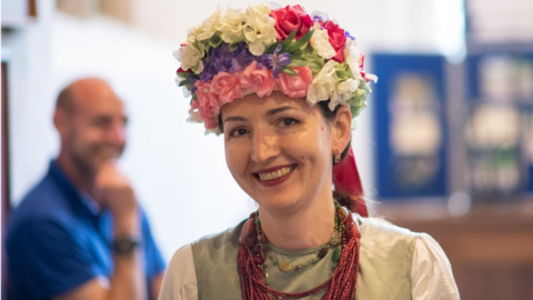 A smiling woman wearing a dress and colourful headdress made of flowers