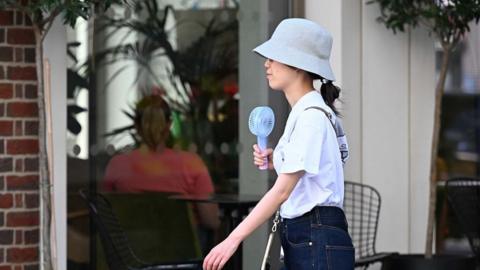 Woman holding fan and wearing hat on a London street
