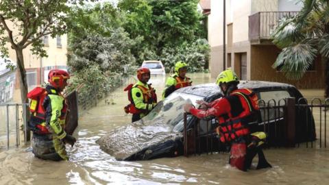 Firefighters work next to a flooded car, after heavy rains hit Italy's Emilia Romagna region