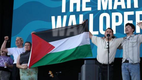 Band members from the Mary Wallopers protest on stage at the Victorious Festival in Portsmouth with a Palestinian flag.