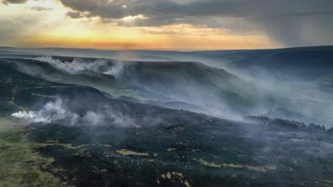 Shot of rolling moorland hills which are blackened and smoking