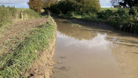 A country road with a large flood and very muddy banks.