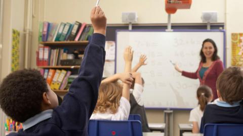 Children raising hands in classroom - stock photo
