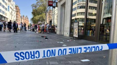 A blue and white police tape in front of the scene where the attack took place, with bits of material, a cap and a lighter visible on the ground