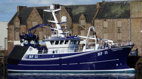 The Fortitude BF 11 fishing boat. The vessel is mostly a deep blue colour with white sections. It has docked in a harbour.