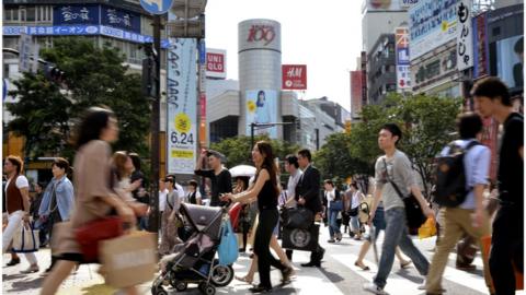 Pedestrians cross a road in front of the Shibuya station in Tokyo