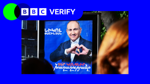 Street poster of a man wearing a blue suit doing a heart sign with his hands inside a blue BBC Verify frame