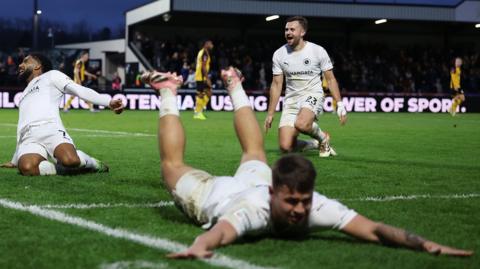 Boreham Wood's Matt Rush dives full length across the pitch with arms outstretched after scoring against Newport County