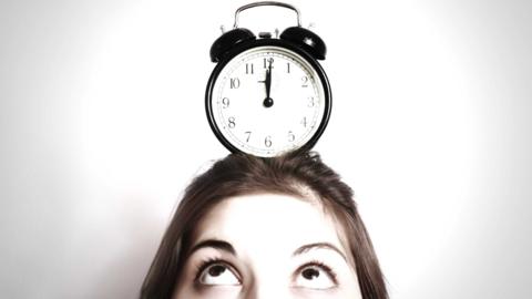 The top of a head with eyes looking up at a traditional analogue alarm clock