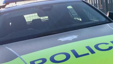 A West Yorkshire Police car with blue lights and "POLICE" written in blue on the front on a fluorescent yellow background.