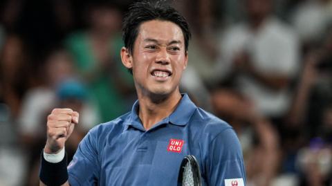 Japan player Kei Nishikori, in a blue polo shirt, pumps his fist on a tennis court, blurred crowd behind him