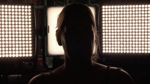 A silhouette of a woman, with bright lights behind her. She is not identifiable.