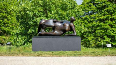 Henry Moore's statue Reclining Woman: Elbow on a patch of grass next to a path.