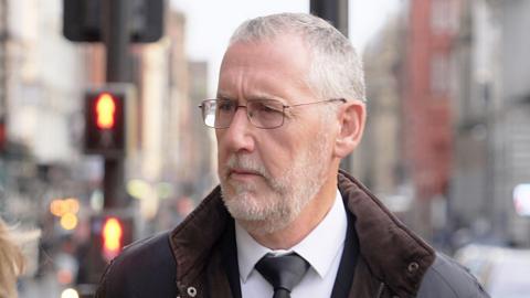 Ian Harvey arriving outside the venue, wearing glasses, coat and tie