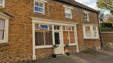 A two-storey brick cottage with white sash windows and a white window-framed door facade