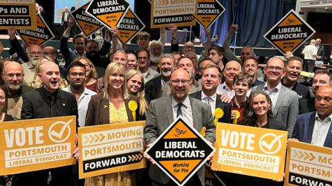 A group of Liberal Democrats celebrating with bright yellow signs