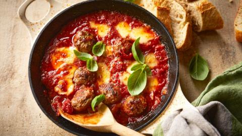 Top down view of a pan with fennel and chilli meatball bake. A wooden spoon is in the side of the dish.