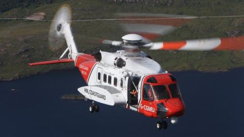 A red and white coastguard helicopter flies over the sea 