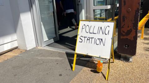 A picture outside Beau Sejour Leisure Centre. There is a yellow road sign with "Polling station" written on it in capital letters.  