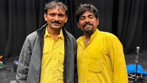 Asin and Sawai smiling at the camera. They are both wearing yellow. They have brown hair. Asin is wearing a grey jacket.