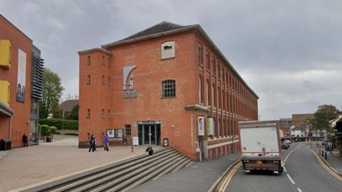 A large red brick converted factory building on a town centre road