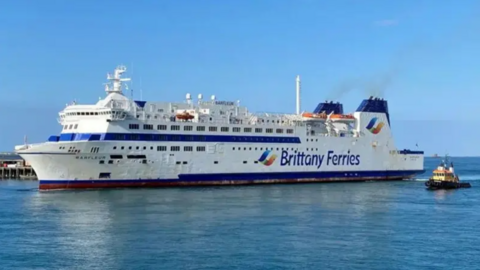 A white ferry with blue tipped chimneys with the words Brittany Ferries on the side arriving in St Peter Port Harbour.