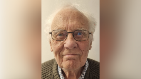 John Burdon has glasses and short white hair.